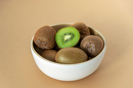Kiwi fruits in a white bowl on beige background. Healthy food concept. Close up.