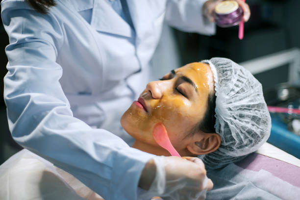 la cosmetologa asiatica cinese sta applicando umidità sul viso del paziente per il trattamento del viso - scrub brush immagine foto e immagini stock