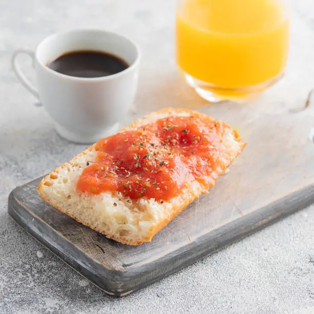 Photo of Pa amb tomaquet or tomaca (bread with tomato) classic snack in Catalan and Spanish cuisine, eaten for breakfast with cup of coffee and orange juice