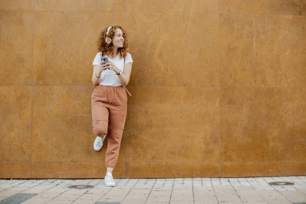 istock Young girl leaning against a wall uses a mobile phone 1311111788