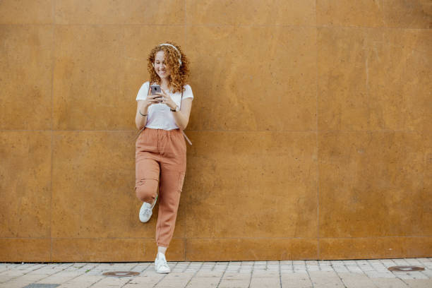 istock Young girl leaning against a wall uses a mobile phone 1311111907
