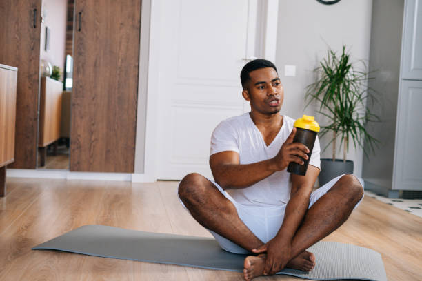 istock African-American man sitting cross-legged and relaxing on exercise mat after workout, drinking water 1311112049