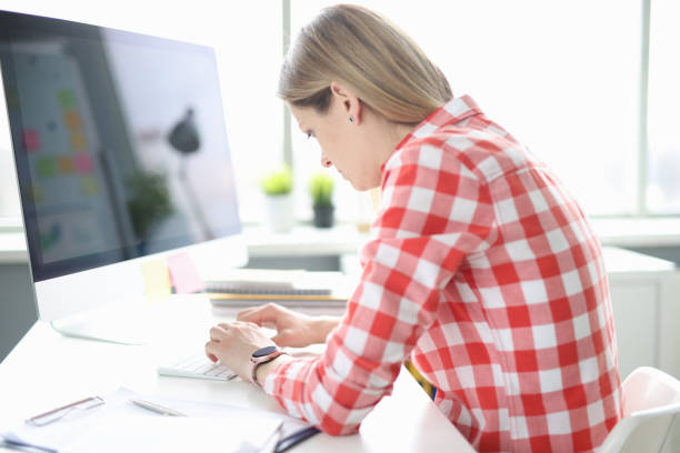 Young woman works at computer with crooked back Young woman works at computer with crooked back. Posture and spine problem from sedentary work concept bad posture stock pictures, royalty-free photos & images