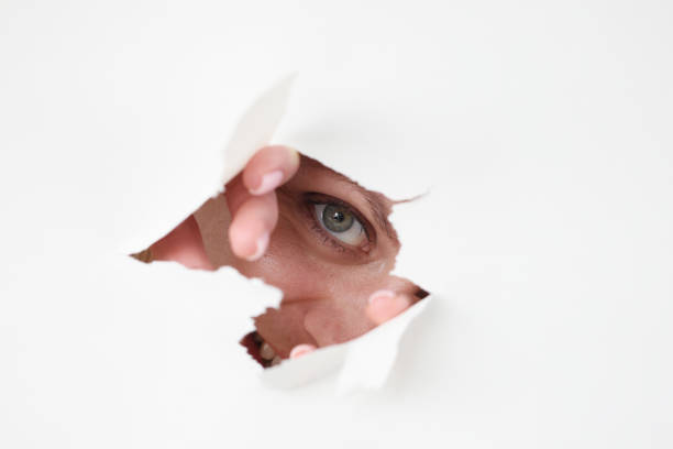 istock Woman eye looks through hole in white paper 1311112430
