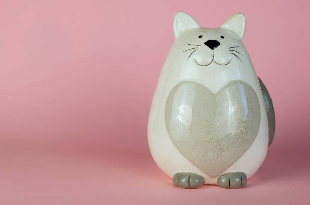 Cat piggy bank on a pink background. Gray ceramic cat-shaped penny bank. Side view. Copy space
