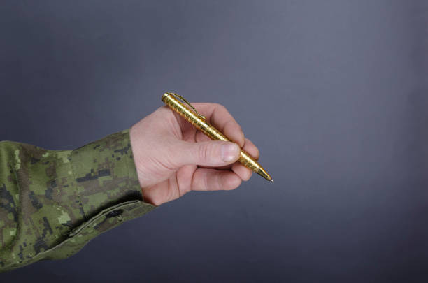 istock Man in camouflage uniform is holding pen against gray background 1311112489