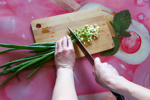 Woman cuts green onions on a cutting board, first person view
