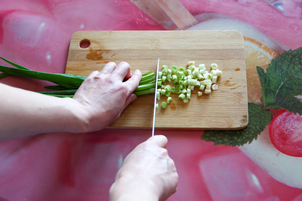 Woman cuts green onions on a cutting board, first person view