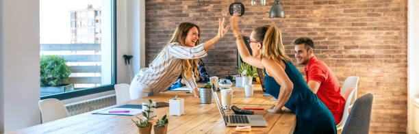 Business women celebrating a success high-fiving in the office Business women celebrating a success high-fiving hands in the office corporate culture stock pictures, royalty-free photos & images