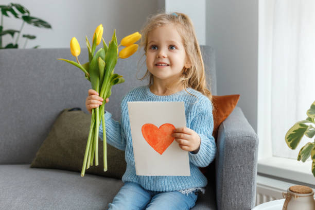 国際女性と母の日。彼女のママのために赤いハートと手の黄色の花とはがきを持つ小さな巻き毛の女の子。かわいい娘の肖像。家族の休日おめでとうございます。 - love flower single flower letter ストックフォトと画像