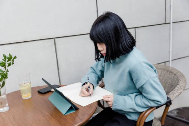 istock Asian woman are sitting thinking and writing with pen and open notebook while using digital tablet 1311122329