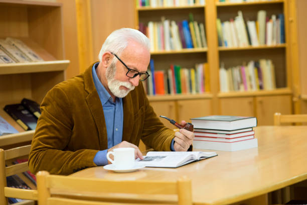 istock Senior man reading books in the library 1311124492