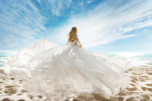 Mujer en la playa con vestido blanco volando sobre el viento. veraneo. Cielo de sol en el mar de Arena de Playa photo