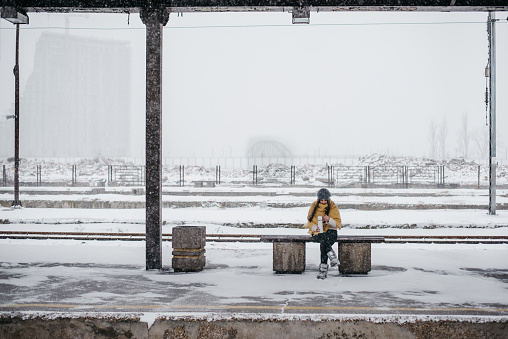 Young woman sitting on a bench waiting for a train at an empty railway station in winter