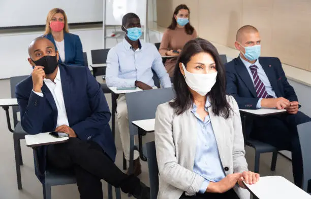 International group of business people in protective masks listening to presentation at tables in boardroom