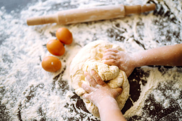 istock Children hands kneading dough on wooden table. Easter baking preparation. 1311134165