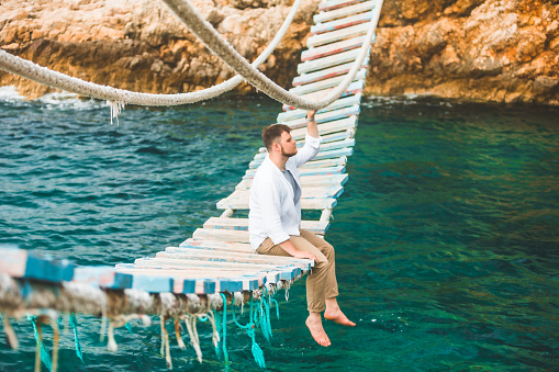 man sitting at suspension bridge enjoying sea view and nature calmness summer time