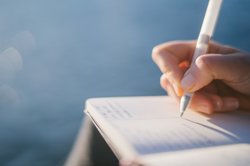 She writes in journal on lakeside pier, Lake Lugano below