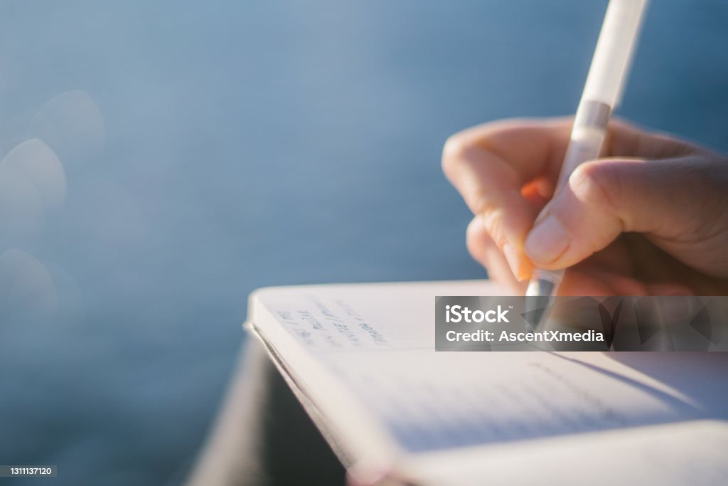 Young woman relaxes by lakeshore in the morning She writes in journal on lakeside pier, Lake Lugano below Writing - Activity Stock Photo
