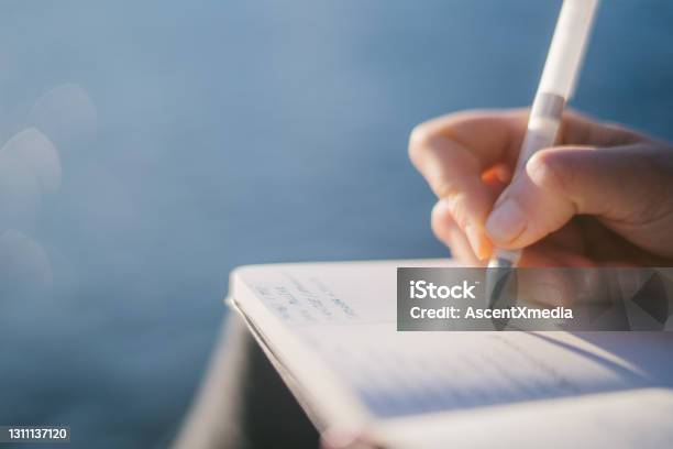 Young Woman Relaxes By Lakeshore In The Morning Stock Photo - Download Image Now - Writing - Activity, Note Pad, Creativity