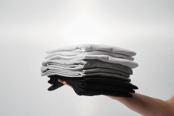 istock Basic outfit. Male hand holding stack of multi colored t-shirts against grey background 1311137424