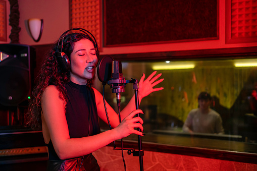 Young female singer recording song in professional music studio
