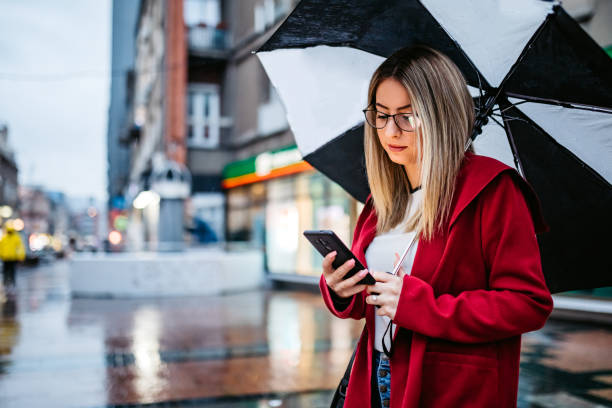 istock Woman texting on phone under umbrella in the rain 1311142362