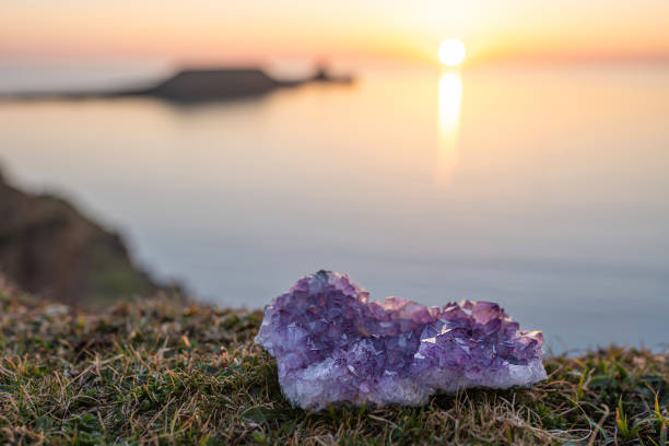 Single raw amethyst gemstone on grass with sea at sunset background Amethyst crystal druse laying on grass with sea at sunset background with copy space. Single raw natural purple geode outdoors rhossili bay stock pictures, royalty-free photos & images