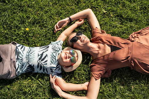 Happy family: mother and child son laughing, lying on the green grass in nature. Summer time. Real people emotions, joy concept.