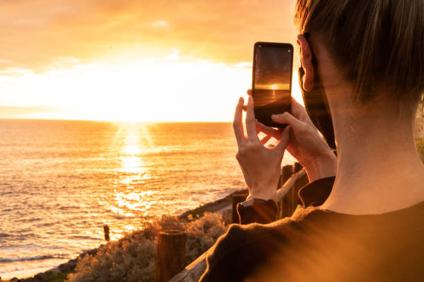woman holding mobile phone and taking photo of an amazing sunset view over sea. - 19636 imagens e fotografias de stock