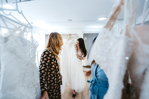 Young Caucasian beautiful woman trying wedding dress with her two best friends.