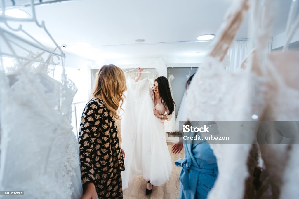 Trying wedding dress Young Caucasian beautiful woman trying wedding dress with her two best friends. Wedding Dress Stock Photo