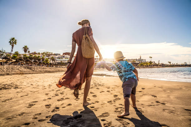 familievakantie op tenerife, spanje. moeder met zoon die op het zandige strand loopt. - canarische eilanden stockfoto's en -beelden