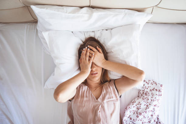 Desperate girl suffering insomnia trying to sleep Young beautiful Caucasian woman on bed having headache / insomnia / migraine / stress. Young woman covering her face with hands. Desperate girl suffering insomnia trying to sleep infamous stock pictures, royalty-free photos & images