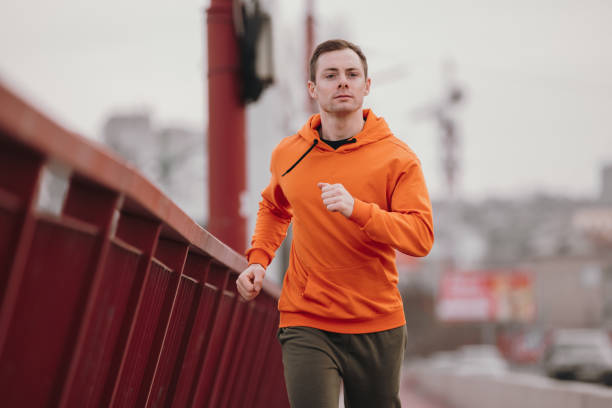 istock Man in orange hoodie running fast on a bridge 1311152647
