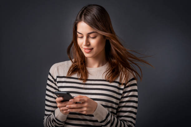 istock Smiling young woman text messaging while standing at isolated dark background 1311157277