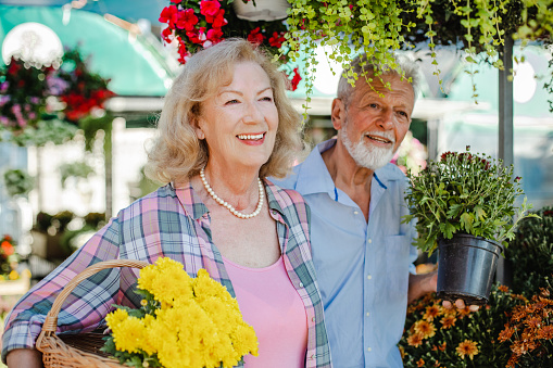 A happy and smiling senior couple is baying plants for their garden on the farmers market