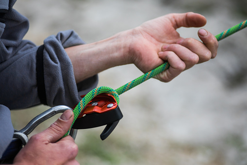 Close up shot of a man's hands operating a rock climbing belaying device.