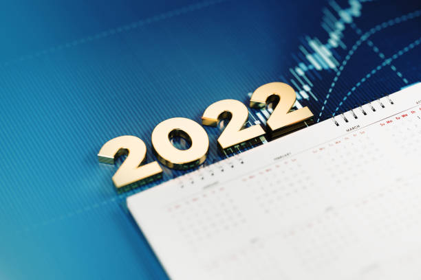 Gold colored 2022 sitting over a white calendar on blue financial graph. Horizontal composition with selective focus and copy space. Investment, stock market data and financial planning concept.