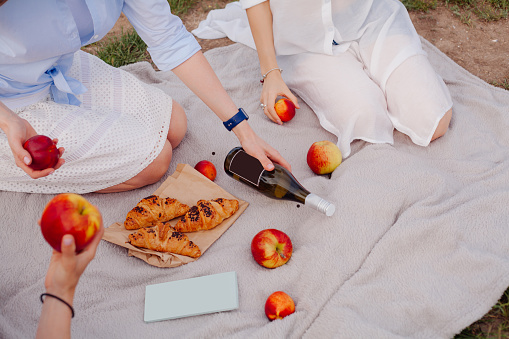 girls at picnic surrounded by apples, wine and croissants