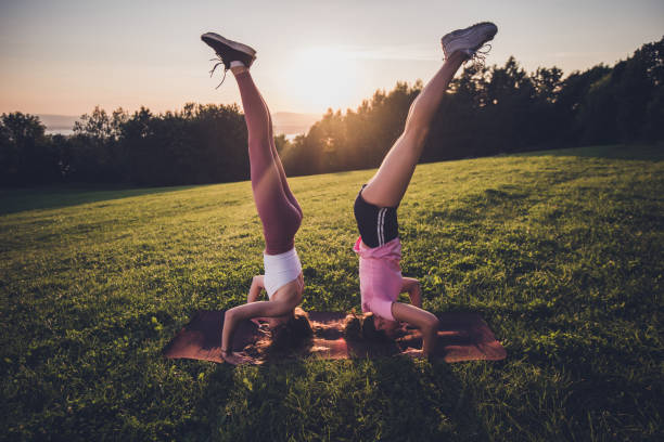 Two young women doing double yoga asana supported headstand.