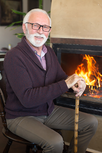 Smiling senior man sitting in front of the fireplace at home.