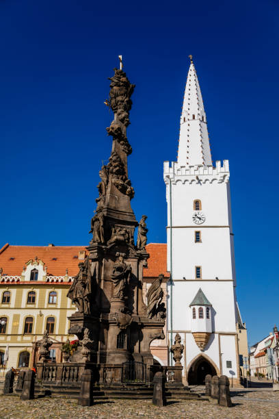 istock Holy Trinity Column with baroque sculptural group, Main town Peace square, gothic city hall tower, Medieval renaissance historical buildings, arcade, sunny day, Kadan, Czech Republic, April 04, 2021 1311173224