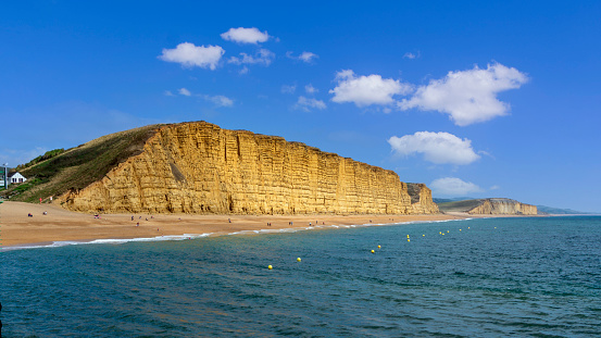 April 7th. 2021.People on beach in front of a huge cliff on a sunny day in Spring. Bridport West Bay, Jurassic coast, Dorset England UK.