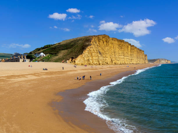 April 7th. 2021.People on beach in front of a huge cliff on a sunny day in Spring. Bridport West Bay, Jurassic coast, Dorset England UK.