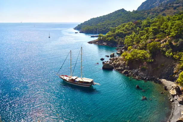 View from the mountain to the blue clean water of Mediterranean Sea with yacht, rocky mountain slopes with pine-trees forest, near Fethiye-Turkey