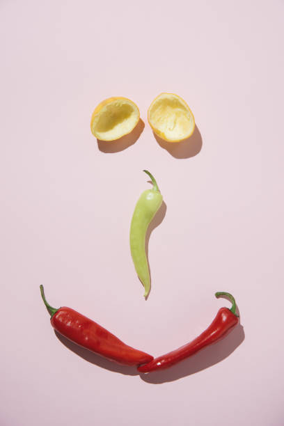 Red and green pepper paprika and two halfs of squezeed lemon on light pink background centered forming a cheerfully smiling peaceful face. Flat lay minimal nature summer healthy fruit and vegetables vitamin c boost hot food beach on sunlight concept. pimentón de pimiento rojo y verde y dos mitades de limón squezeed sobre fondo rosa claro centrado formando una cara tranquila alegremente sonriente. flat lay minimal nature verano frutas y verduras saludables vitamina c impulsar la playa de alimentos cal