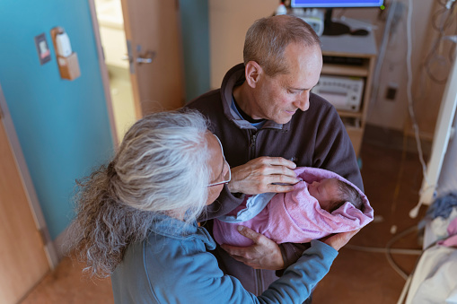 A beautiful moment that shows a mixed race asian grandmother and her caucasian husband holding their newborn granddaughter together for the first time in the hospital room.