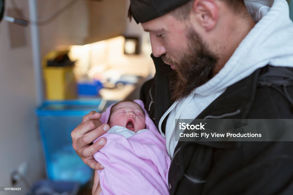 New Father Holding His Newborn Daughter In Hospital After Delivery A young caucasian father in his 30's is holding his mixed race newborn girl in the hospital room. The child was born moments before and he is affectionally marveling at her and snuggling. Baby - Human Age Stock Photo