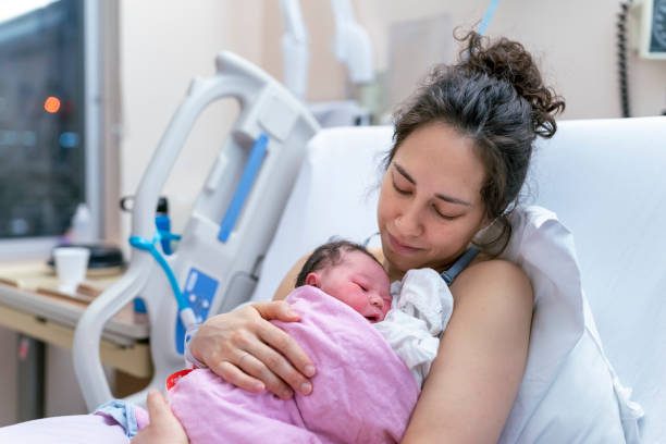 Mixed Race Mother Doing Skin to Skin Bonding with Newborn in Hospital Bed After Delivery A beautiful and relaxed ethnic mother is snuggling her newborn and affectionately holding her in the hospital after delivery. biracial newborn stock pictures, royalty-free photos & images